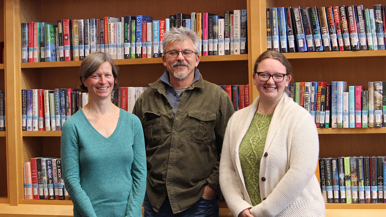 new library staff stand together in front of shelving full of books in the library