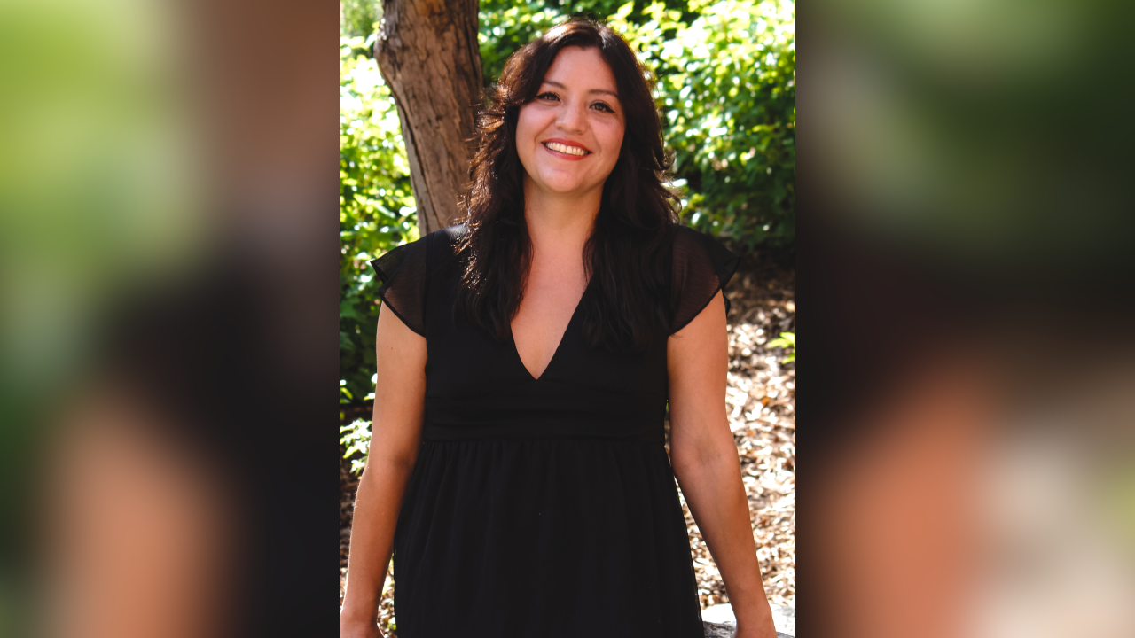 a photograph portrait of a woman wearing a black dress with dark hair standing in front of a tree in the summer