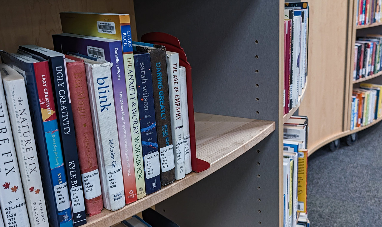 Close-up of a library shelf filled with colorful books, including titles about creativity, psychology, and wellness.