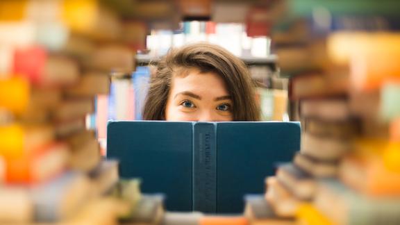 young woman looking through diamond shaped gap in library books