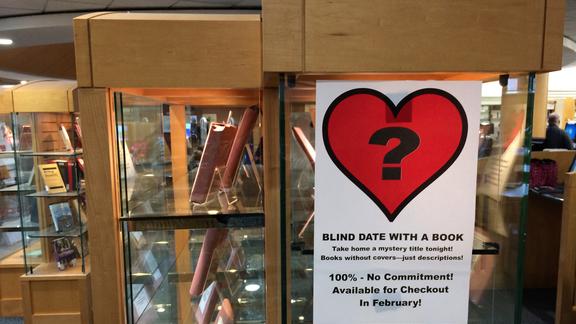 library display case showing books wrapped and sign with question mark inside heart 
