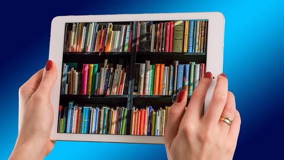 hands of a woman holding an ipad. books spines on a shelf are displayed on the ipad