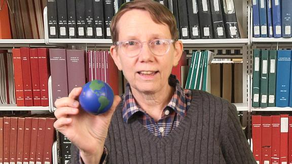 Mags David holding a small globe in front of bookshelves