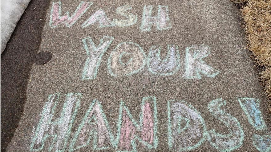 a photograph of a sidewalk that has "wash your hands!" written on it in sidewalk chalk
