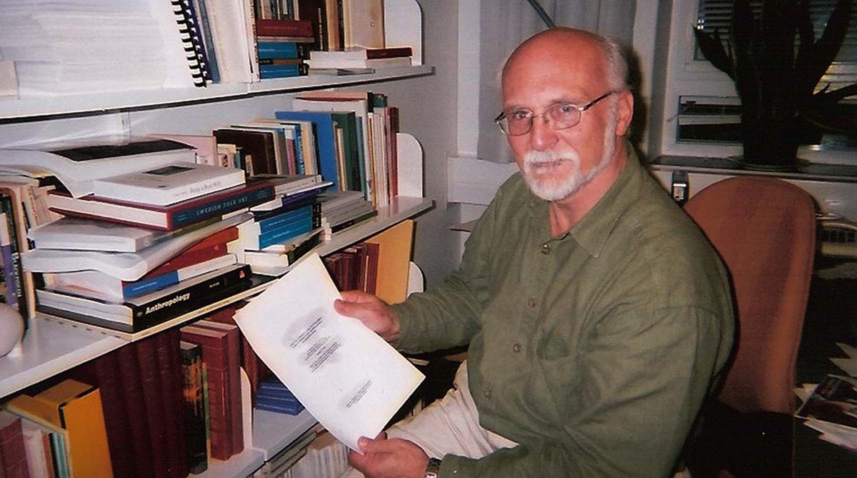 Hugh Beach holding papers at his desk