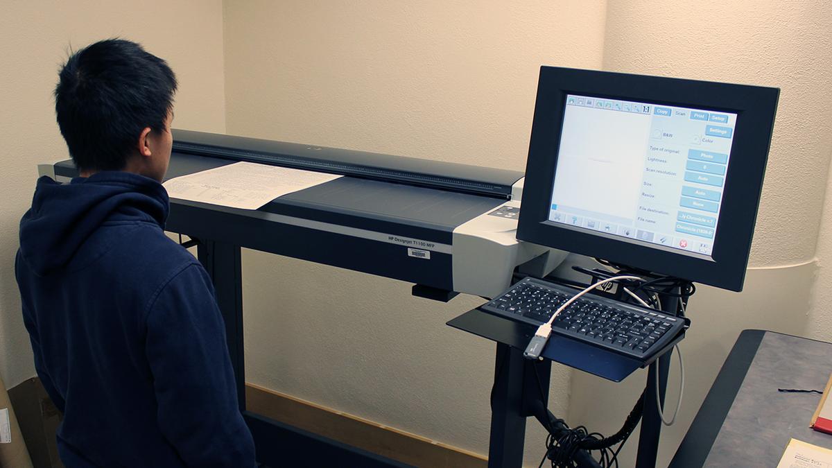 a student scans an old UMD student newspaper on a large format scanner 